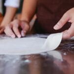 Dłonie formujące ciasto na pizzę na oprószonym mąką blacie