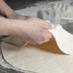 Dłonie wyrabiające ciasto na pizzę na oprószonym mąką blacie