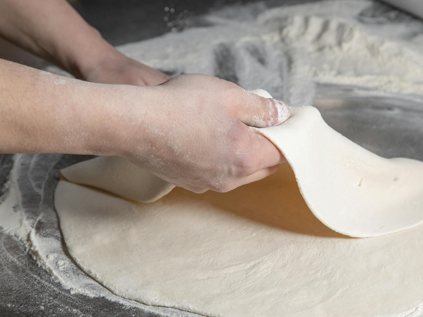 Dłonie wyrabiające ciasto na pizzę na oprószonym mąką blacie