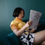 Kobieta na turkusowej sofie rozwiązuje krzyżówkę w nowoczesnym wnętrzu