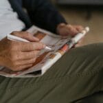 Starsza osoba rozwiązuje krzyżówkę w gazecie długopisem