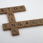 Drewniane płytki Scrabble układające się w napis Stop Think Engage