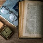 Stare książki, zegarek kieszonkowy i okulary leżące na drewnianym stole