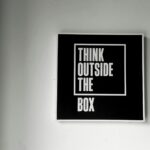 Czarno-biały napis Think Outside the Box jako plakat na ścianie