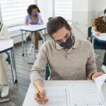 Studenci w maseczkach piszący egzamin w sali podczas pandemii