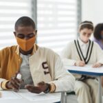 Studenci w maseczkach w klasie używają płynu do dezynfekcji rąk
